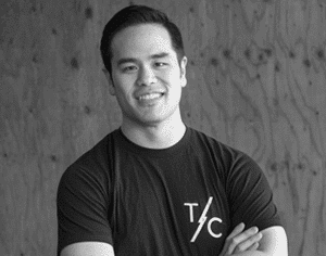 A man in a black t-shirt is standing with his arms crossed and smiling.