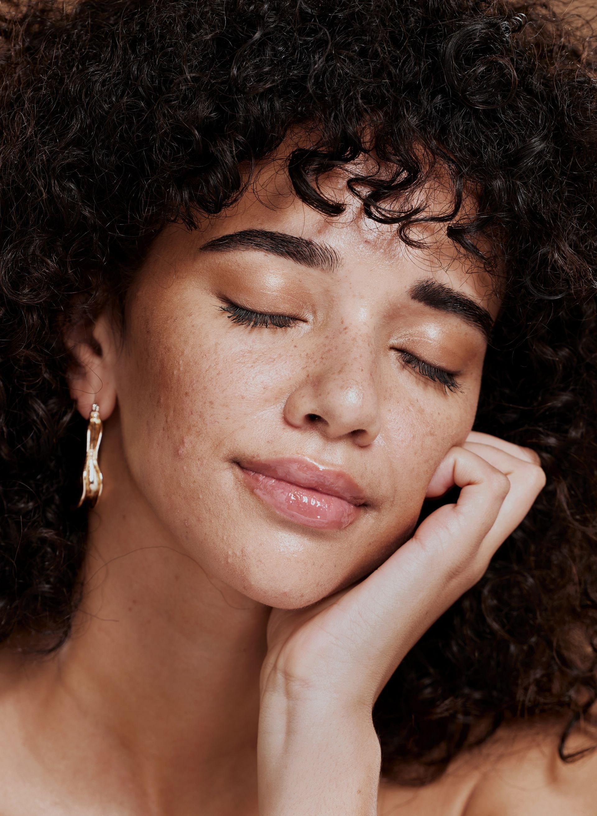 A close up of a woman 's face with her eyes closed and her hand on her face.