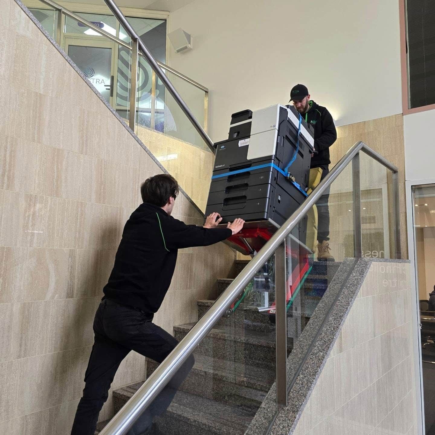 People Moving Stacked Equipment Up an Indoor Staircase With a Handrail — Little Green Removals Geelong in Breakwater, VIC