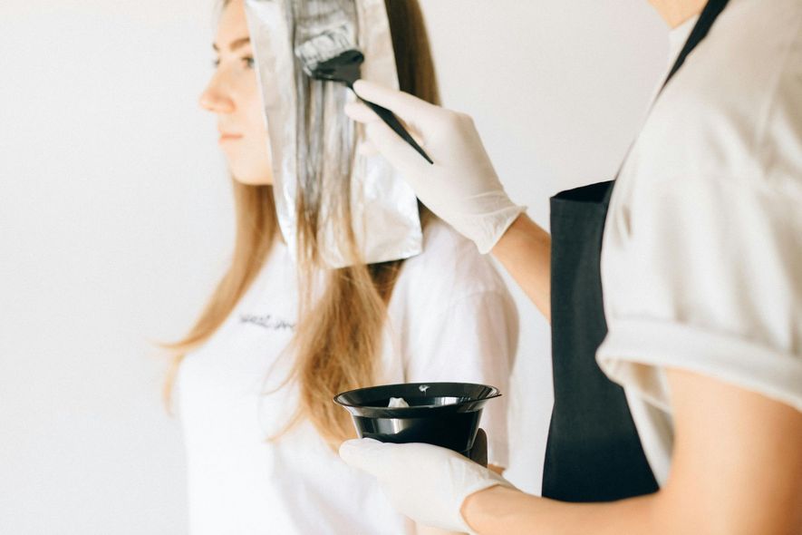 Person getting hair highlighted in a salon, with foils, dye, and brush.