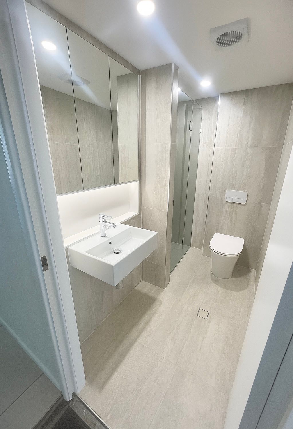 Modern bathroom with a floating sink, toilet, and shower stall. Neutral tones.