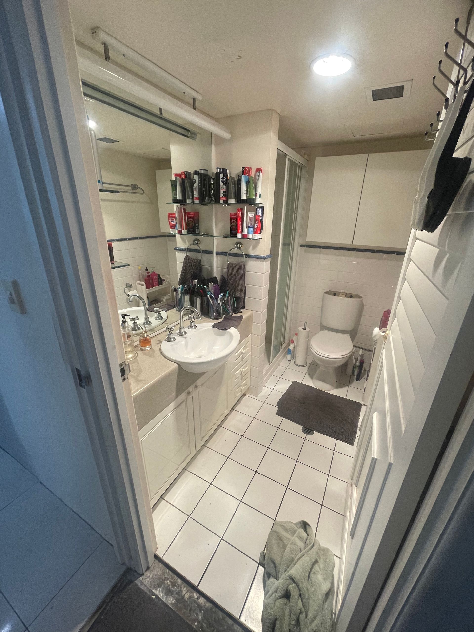 Small bathroom with a sink, toilet, and shower. White tile floor and walls.