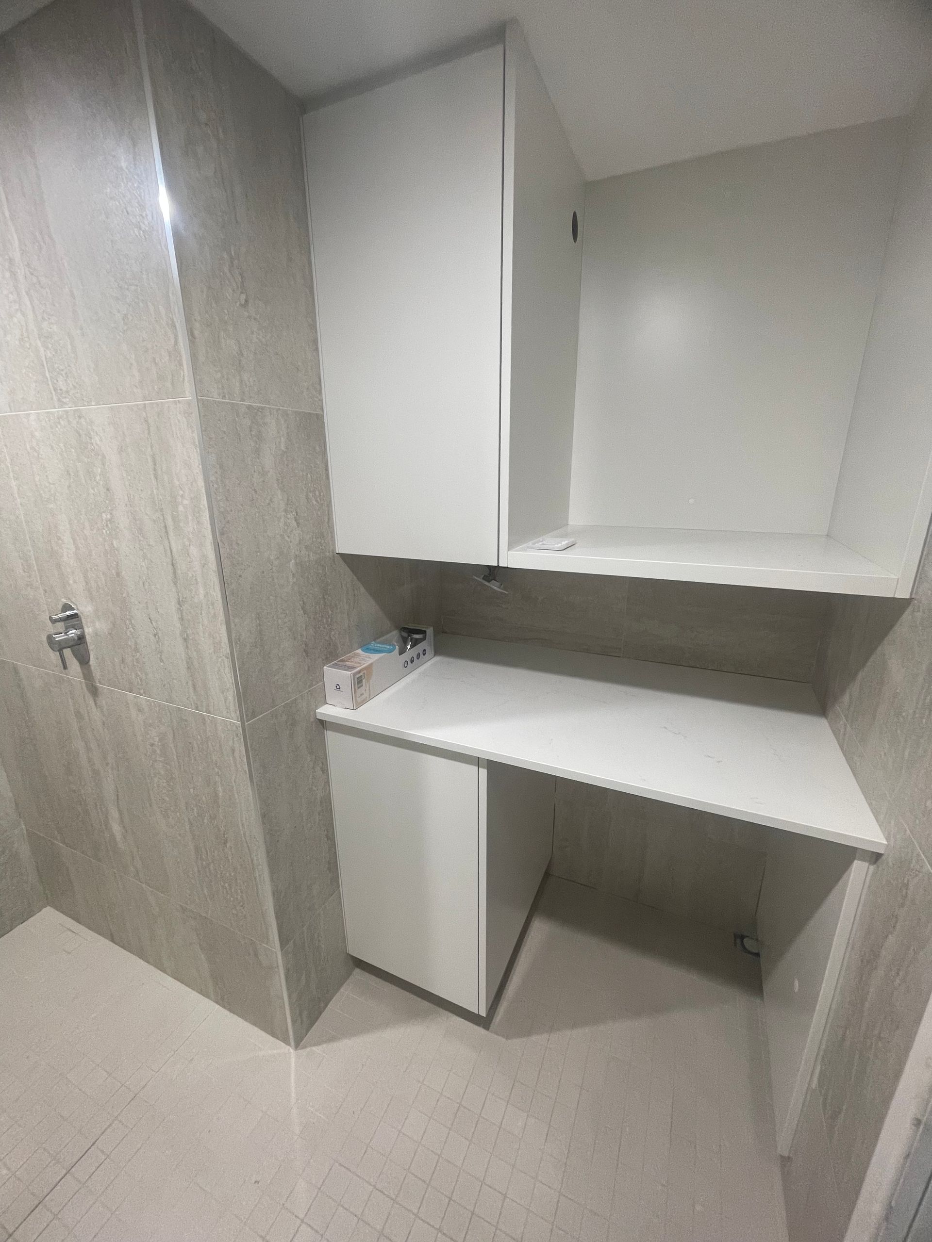 White built-in bathroom cabinets and countertop with a tiled wall.