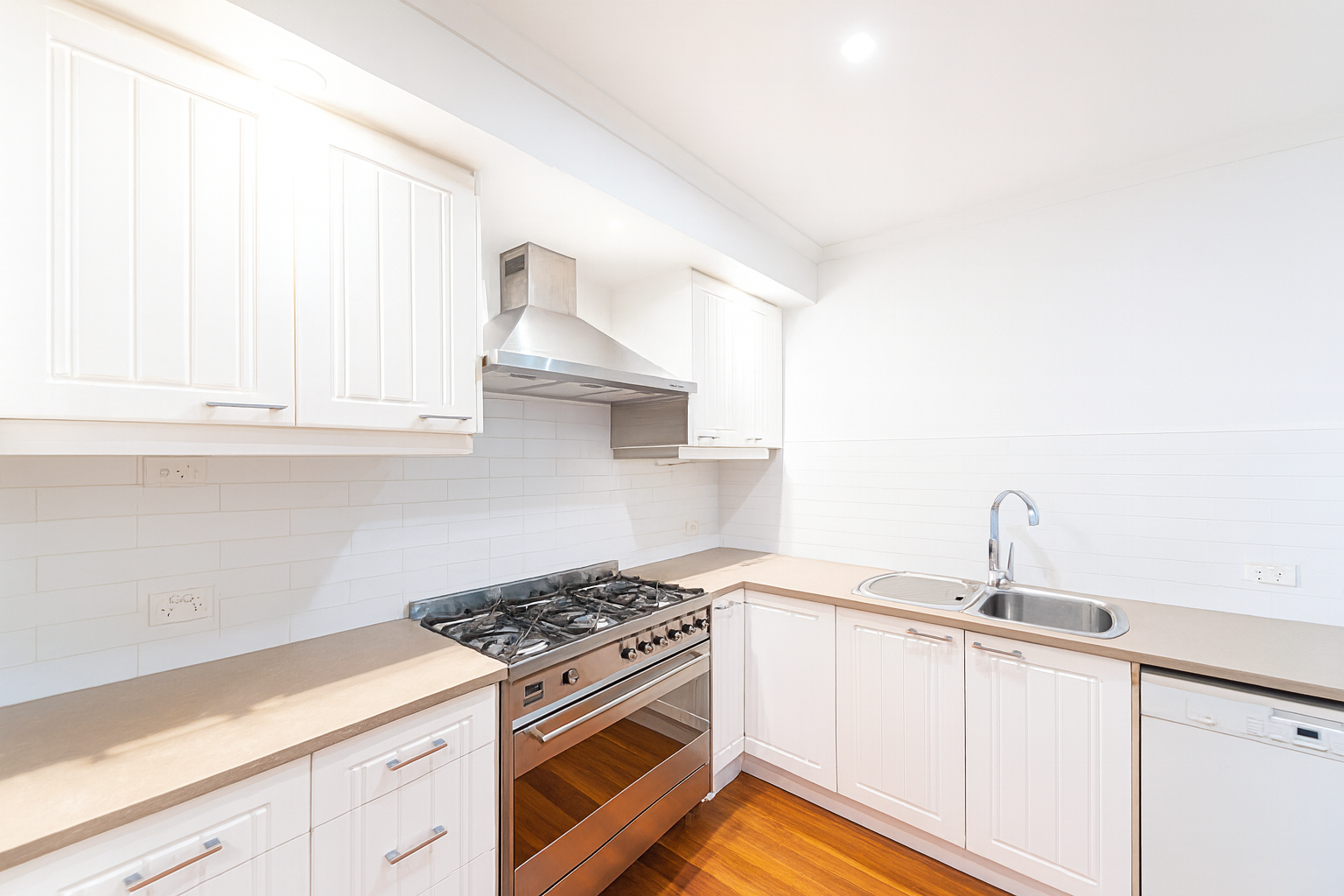 White kitchen with stainless steel appliances, wooden floor, and white cabinets.