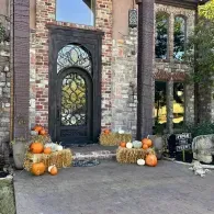Front porch with black wrought-iron door, brick facade, and fall pumpkin decorations.