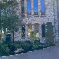 Stone house facade with arched windows, blue shutters, and landscaped front garden