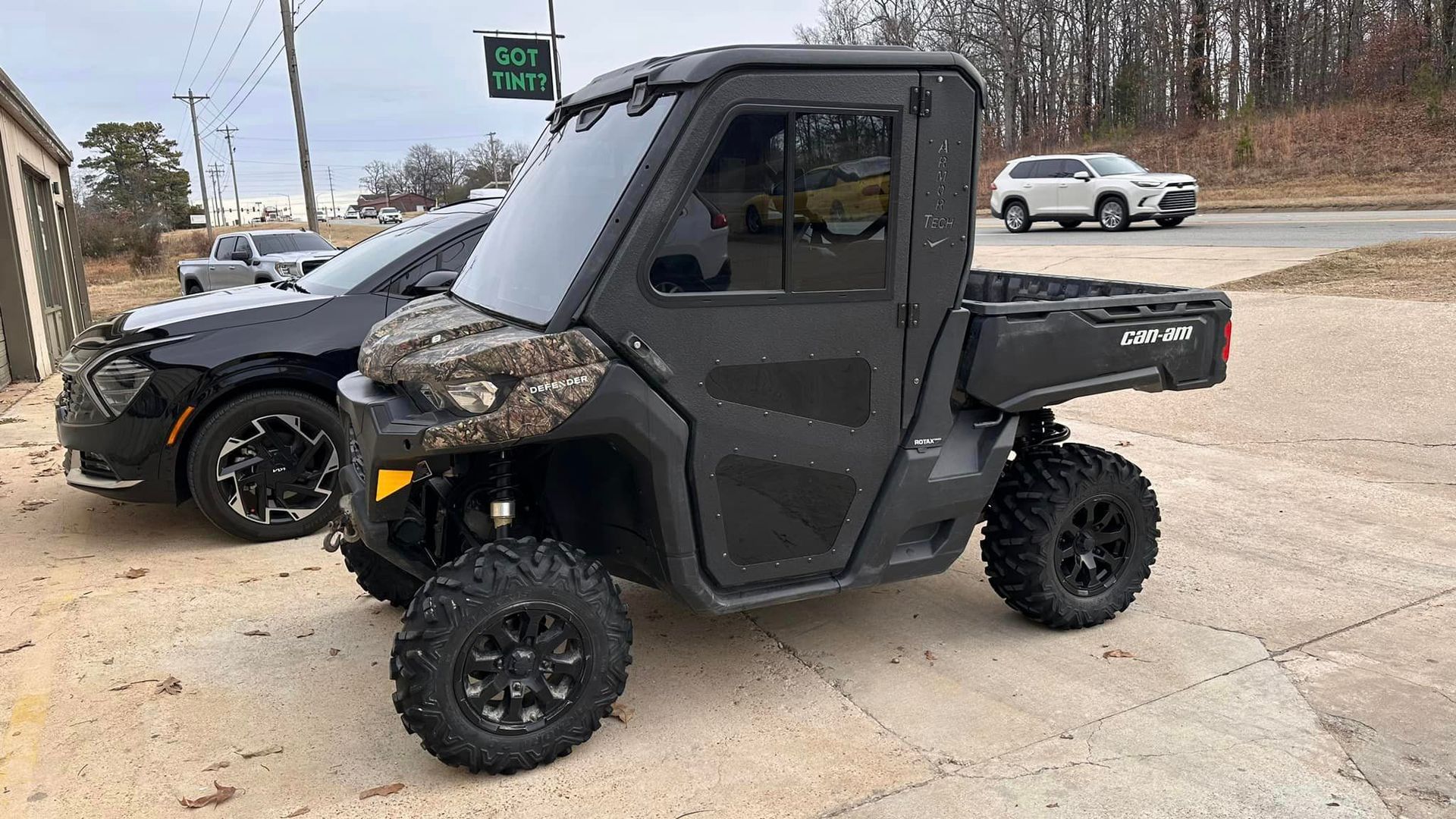 Black side-by-side off-road vehicle parked on a paved roadside with another vehicle behind it.