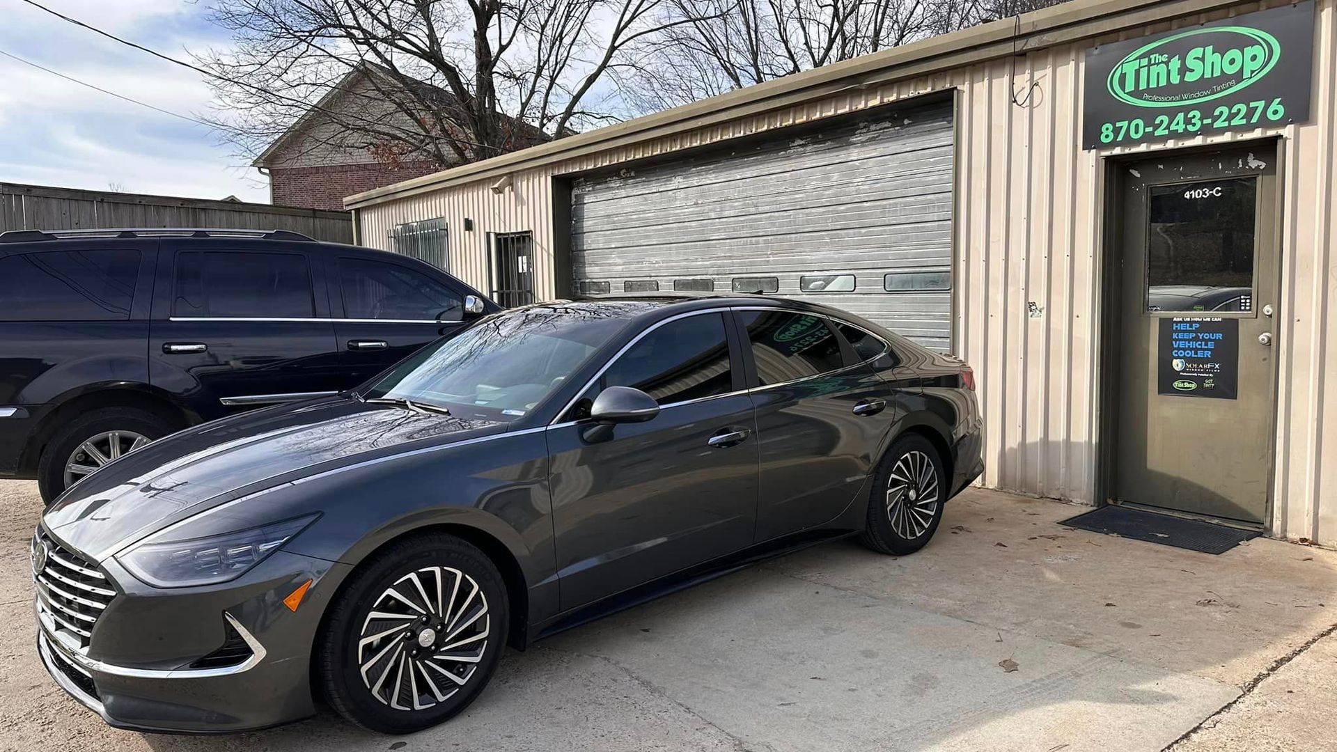Gray sports coupe parked outside a shop with a green sign and garage door