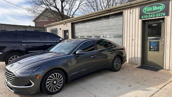 Gray sports coupe parked outside a shop with a green sign and garage door