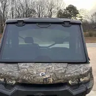 Front view of a camouflaged off-road utility vehicle with a windshield and roof lights outdoors