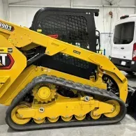 Yellow Caterpillar compact track loader in a garage, showing its side profile and black rubber tracks.