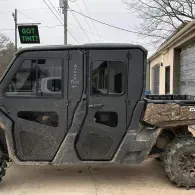 Black Jeep-style off-road vehicle parked beside a house, with muddy tires and a black-and-tan camouflage wrap