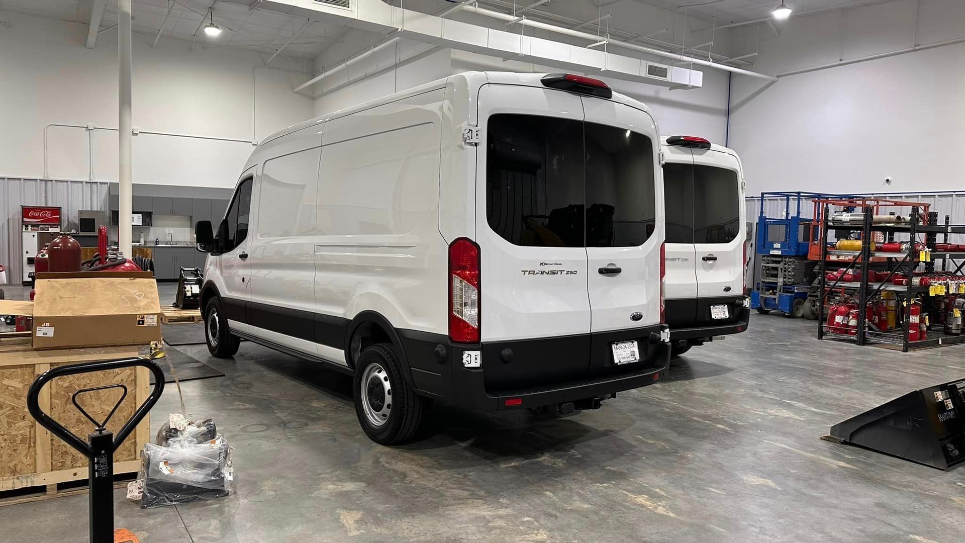 White cargo van in a warehouse garage with shelves, tools, and equipment around it