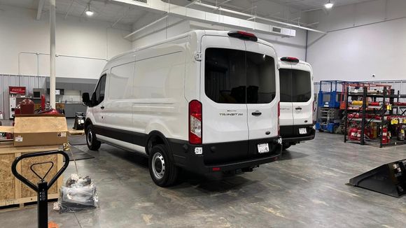 White cargo van in a warehouse garage with shelves, tools, and equipment around it