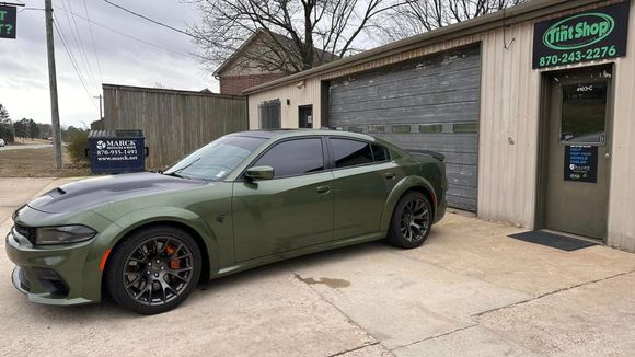 Olive-green Dodge Challenger parked outside a tire shop with a sign and garage door nearby