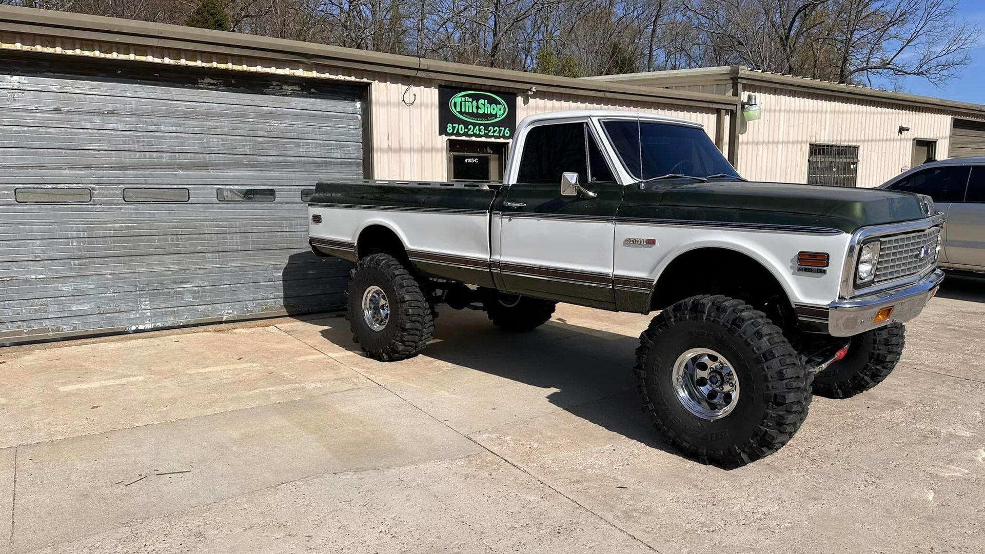 Lifted black-and-silver pickup truck parked in front of a garage on a sunny driveway