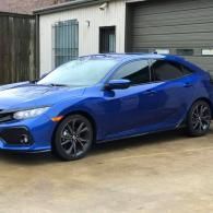Blue hatchback coupe parked in front of a garage on a wet driveway