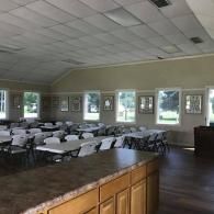 Empty banquet hall with rows of round tables, white tablecloths, and windows along the wall