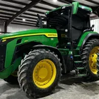 Green and yellow John Deere tractor parked indoors under a metal-roofed shed