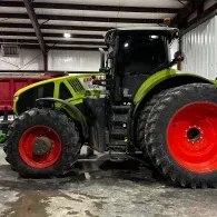 Green and black tractor with red wheels parked inside a metal garage