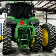 Green tractor with large dual rear tires parked inside a metal garage