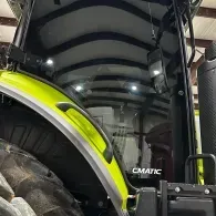 Close-up of a yellow tractor inside a covered barn, showing the large rear tire and cab roof.