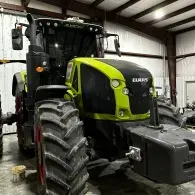 Green Claas tractor with large tires parked inside a workshop