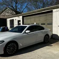 White sedan parked in front of a garage on a sunny driveway