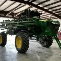Green agricultural sprayer with large tires parked inside a shed
