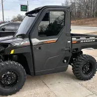 Black off-road UTV with large tires parked outdoors on pavement near a road.