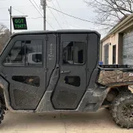 Black side-by-side off-road vehicle parked beside a house, with rugged tires and tinted doors