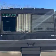Black storefront with a green sign and large window blinds, viewed from across a parking lot.