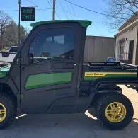 Black-and-green John Deere utility vehicle with yellow wheels parked outside a building.