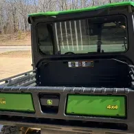 Green utility vehicle cargo bed with black cab and 4x4 badge, outdoors on a road.