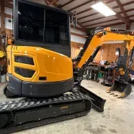 Yellow excavator in a workshop with its arm raised and tracks visible.
