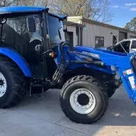 Blue tractor parked beside a building, shown in side view with front loader attached