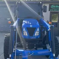 Blue tractor parked in front of a building, viewed from the front.