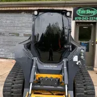 Black skid-steer loader parked outside a shop with a green sign and garage door