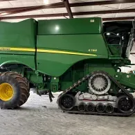 Green John Deere combine harvester with tracks parked inside a shed
