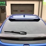 Blue car parked in front of a garage door with rear window and spoiler visible