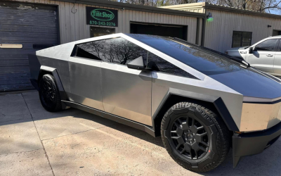Tesla Cybertruck parked outside a garage, shown in side view with a silver body and black wheels.