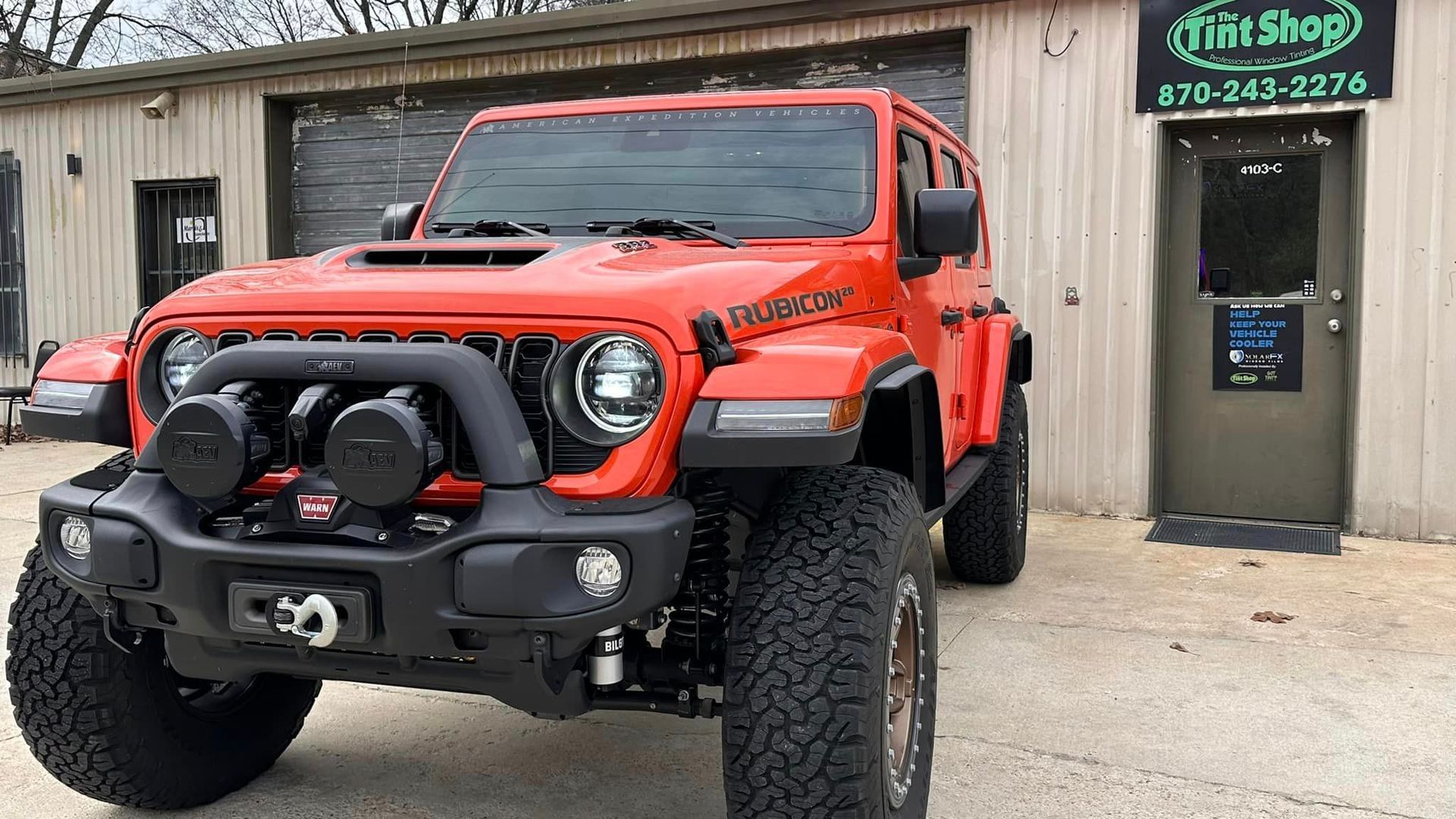 Red Jeep Wrangler parked outside a shop with a winch bumper and off-road tires