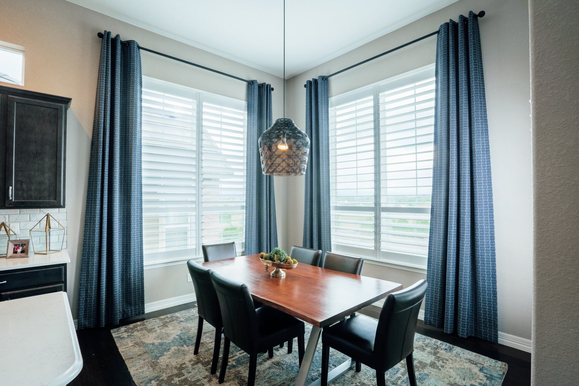 Dining table with black leather chairs in front of gathered blue and white patterned drapery