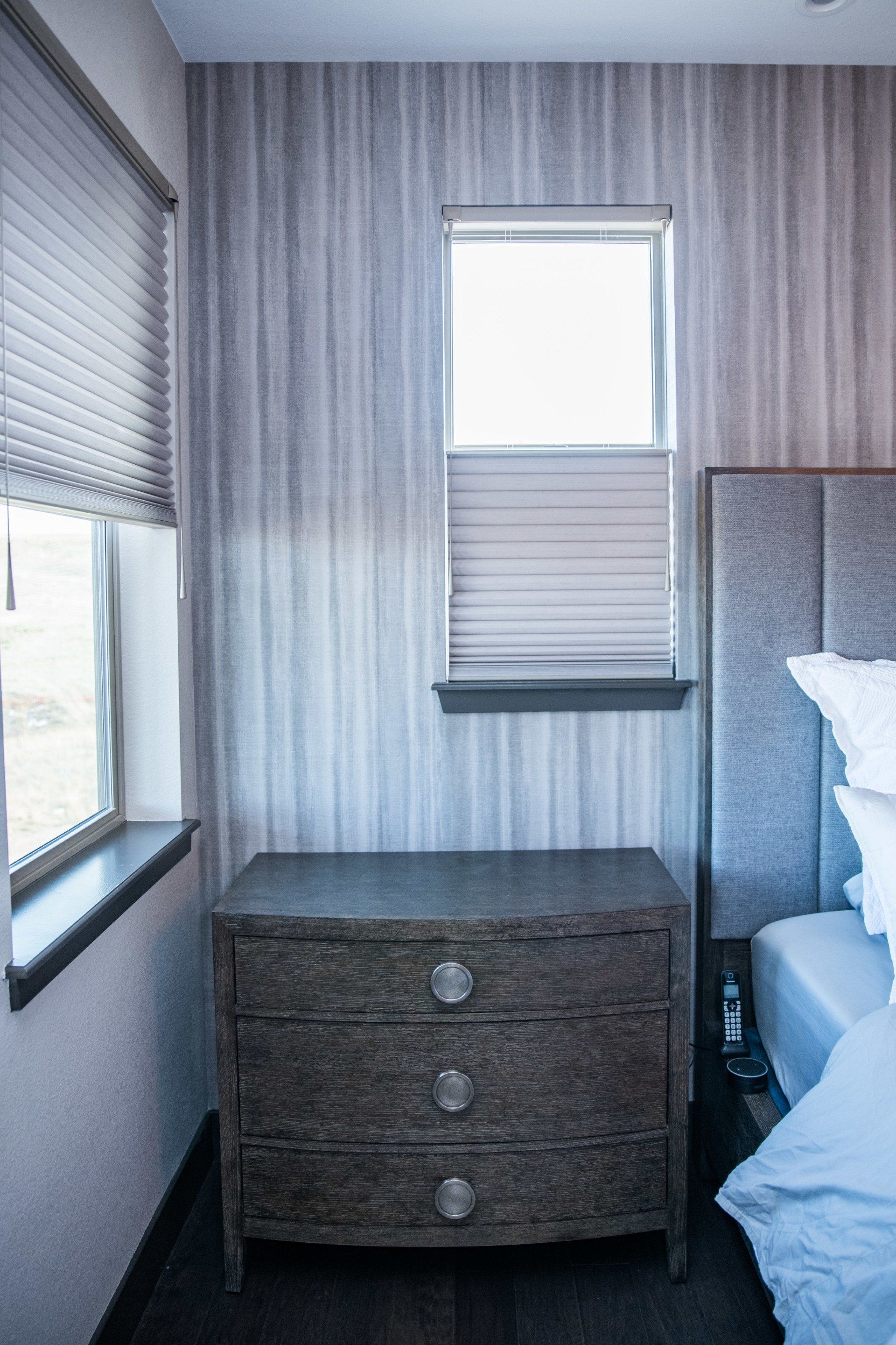 Night stand in front of reclaimed wood wallpaper and a window with a cellular shade