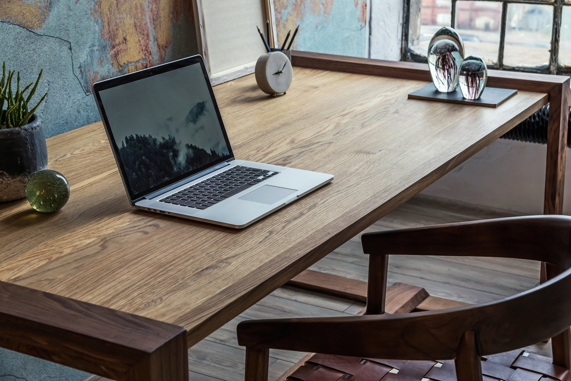 Hardwood table, leather and wood chair, laptop and decorative elements on the surface