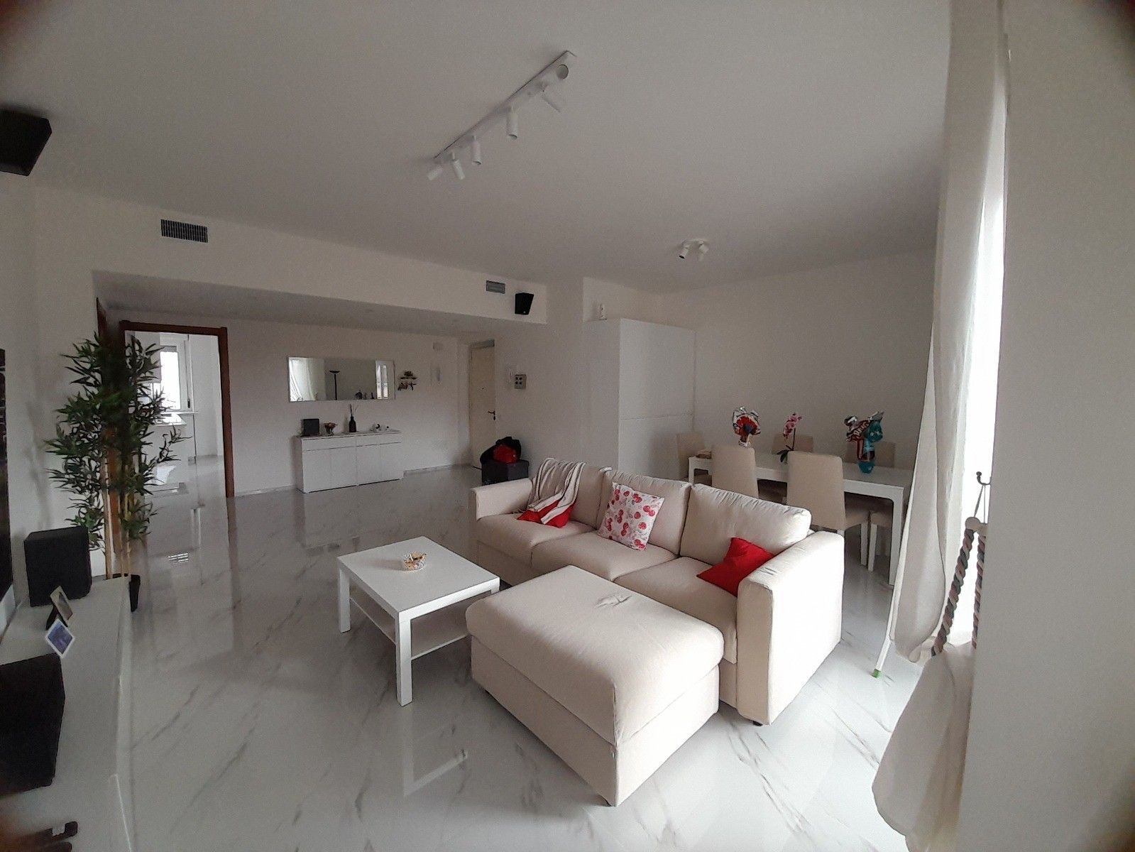 Soggiorno con divano componibile, tavolino e zona pranzo. Pareti e pavimento bianchi.