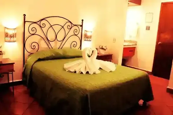 Una habitación de hotel con una colcha verde, un cabecero de metal y dos cisnes hechos con toallas con forma de corazón.