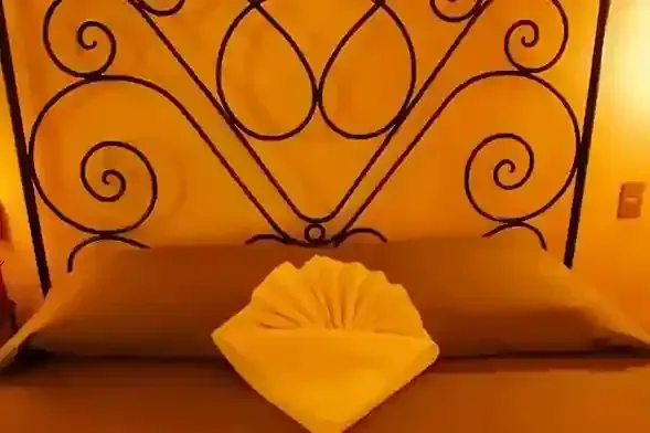 Una cama con una toalla decorativa doblada en forma de abanico sobre la almohada.