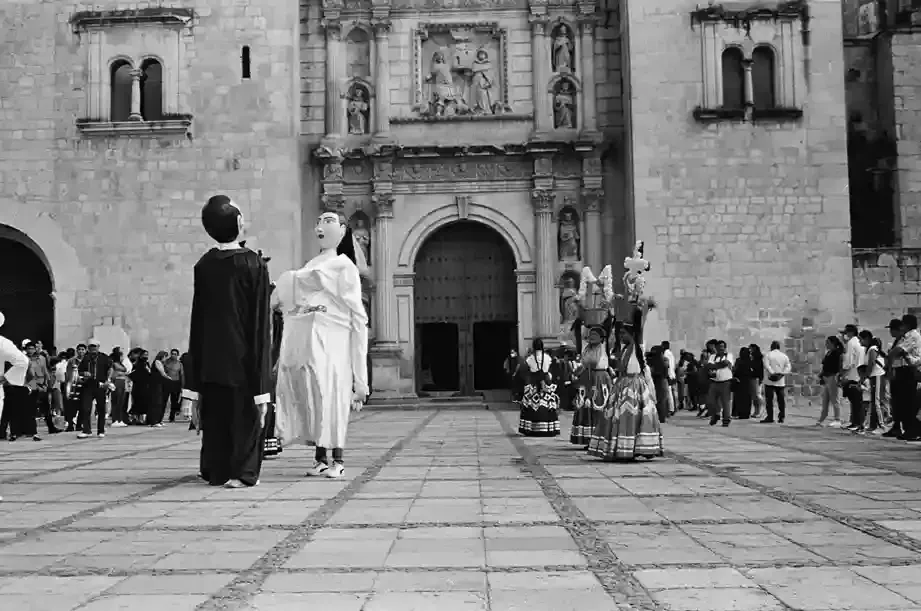 Figuras gigantes con atuendos formales tradicionales actúan frente a una histórica iglesia de piedra.