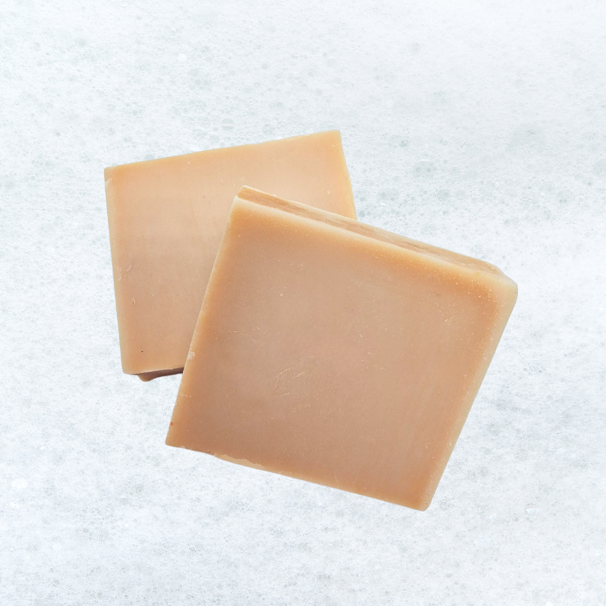 Two squares of soap are sitting on a white surface.